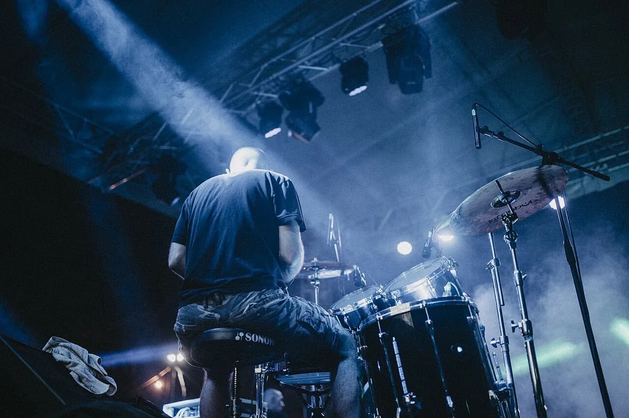 Drummer performing on stage during a live music concert at night with dynamic lighting effects