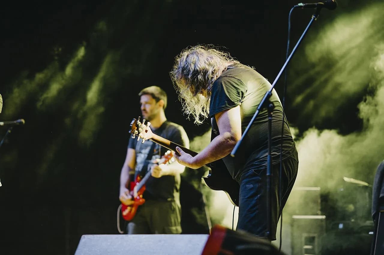 Live rock concert performance featuring musicians playing guitar on stage at night with vibrant lighting effects